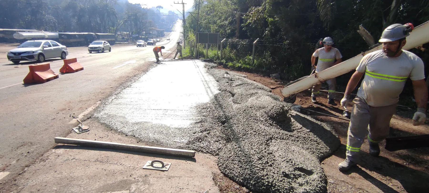 Equipe da Ápice em frente de obra na rodovia: dois profissionais transportam uma régua metálica ao lado do trecho de pavimento de concreto recém-lançado.