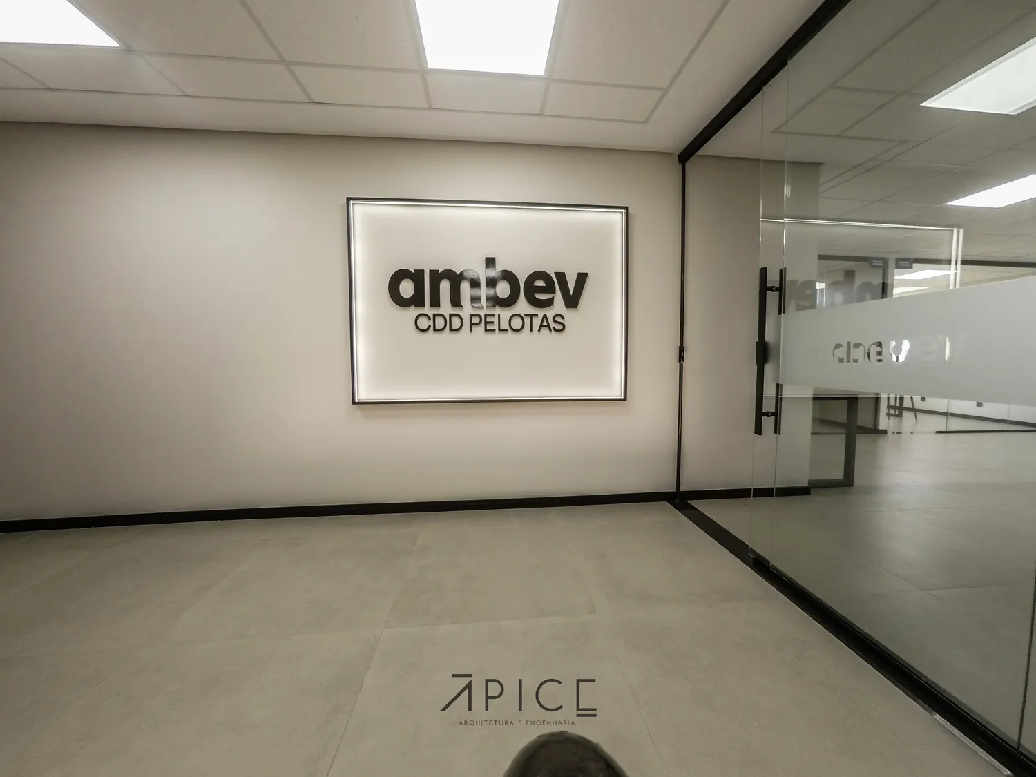 Recepção com letreiro iluminado e divisórias de vidro no centro de distribuição da Ambev em Pelotas.