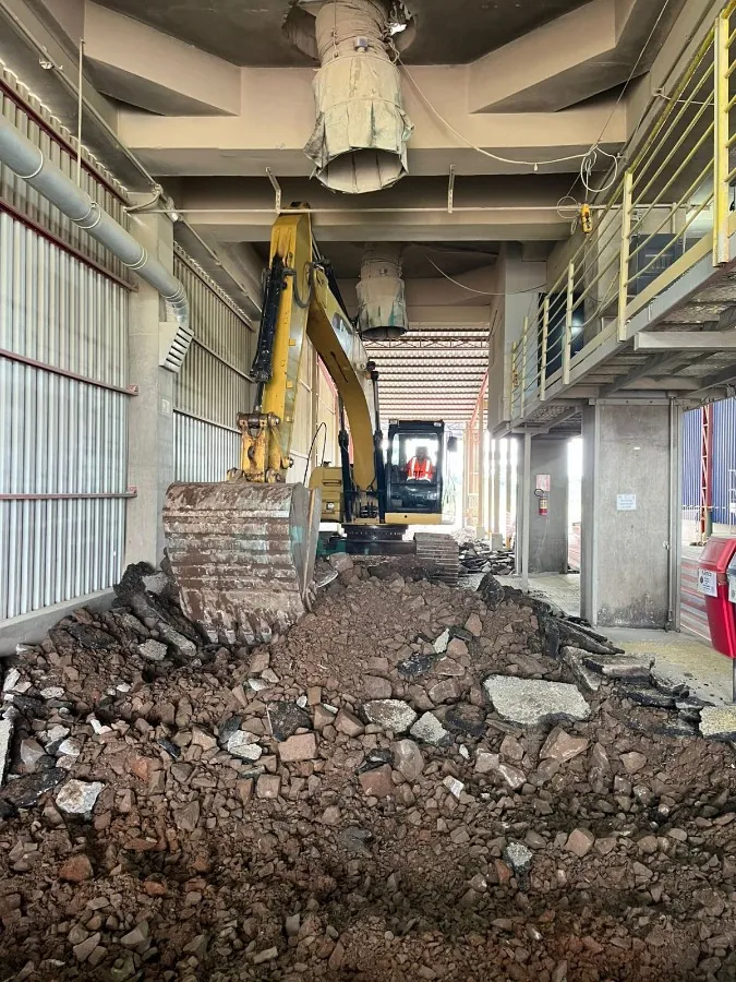 Escavadeira demolindo alvenaria no interior de um galpão, durante a fase de remoção da obra.
